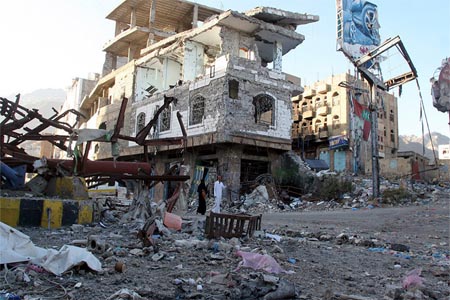 People walk past a building destroyed during recent fighting in Yemen's southwestern city of Taiz
