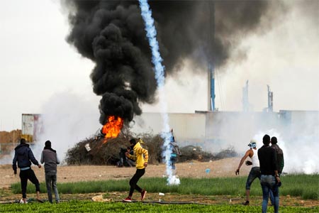 A picture taken on December 10, 2017 shows a tear gas cannister falling amdist Palestinian protesters during clashes with Israeli forces near the Israel-Gaza border.