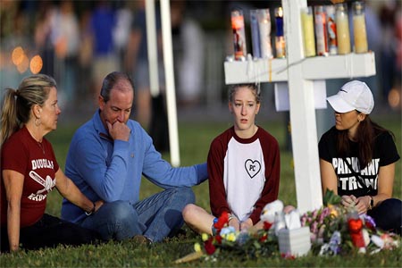 A family sits around one of 17 crosses at a memorial for the victims of the shooting at Marjory Stoneman Douglas High School in Parkland, Florida, U.S. February 16, 2018