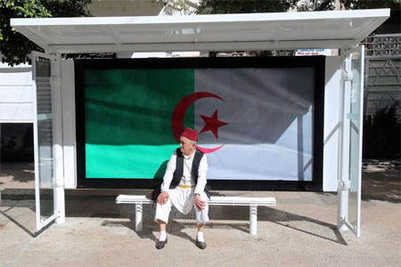 In a quandary. A man sits at a bus station decorated with the national flag in Algiers. (Reuters)