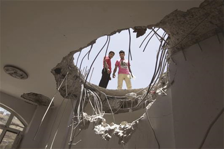 يمنيان يقفان على سطح منزل متضرر جراء غارة لـ «التحالف» على جبل فج عطان (أ ف ب)